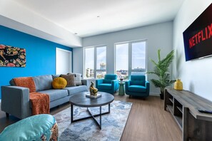 Un soggiorno moderno con un divano grigio, poltrone blu, un tavolino da caffè e un'ampia finestra con vista sulla città.