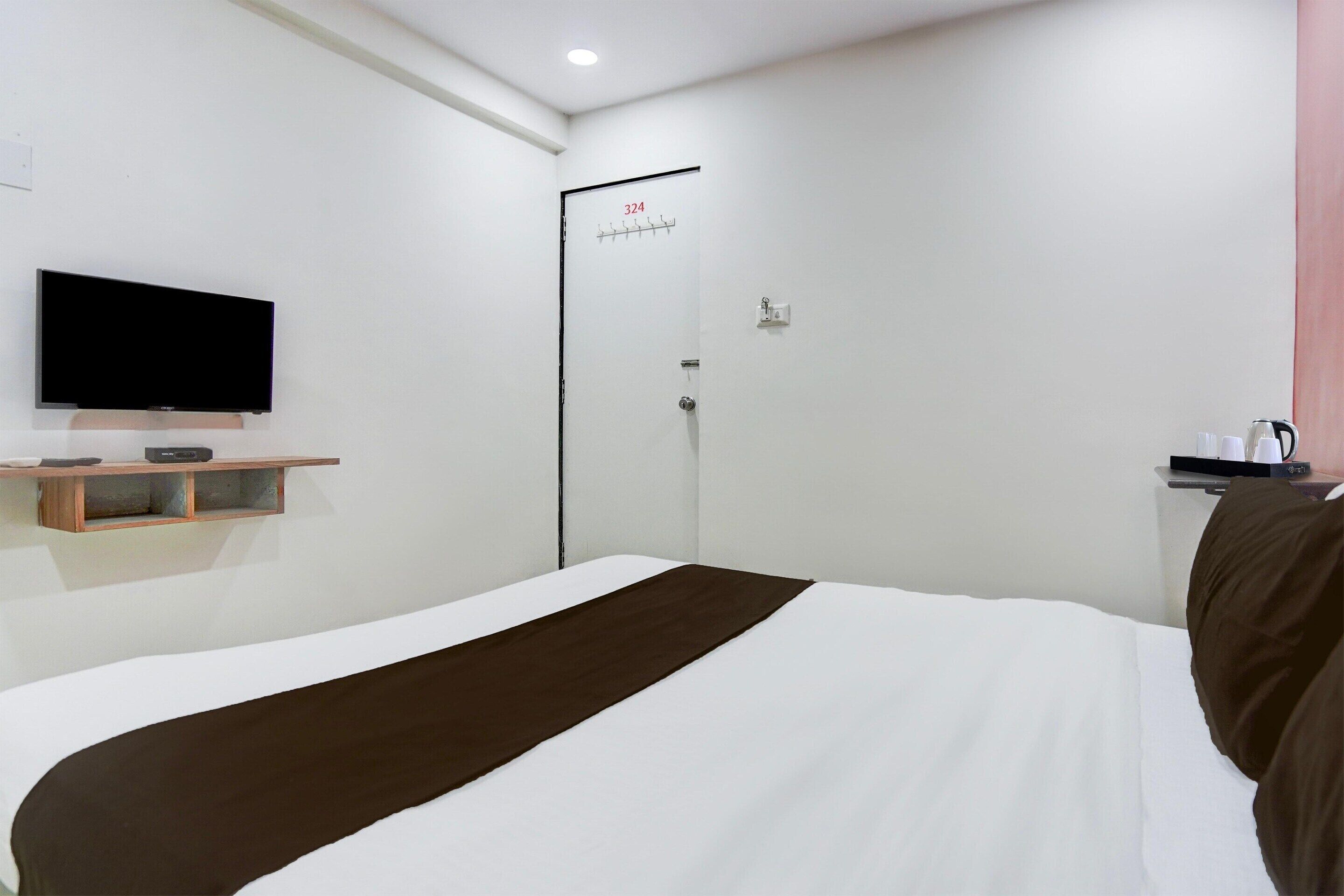 Une chambre d’hôtel avec un lit, un téléviseur posé sur une étagère, une porte avec un numéro et une petite table sur laquelle se trouvent divers objets.