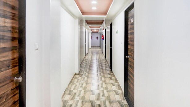 A long, narrow hallway with wooden doors on one side and white walls on the other. The floor has a patterned tile design. - Super Hotel O Dindoli Surat (Surat)