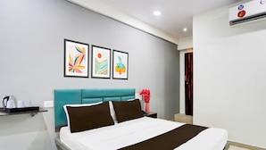 A hotel room with a bed, a nightstand, a wall-mounted air conditioner, and three framed artworks. - Super Hotel O Dindoli Surat (Surat)
