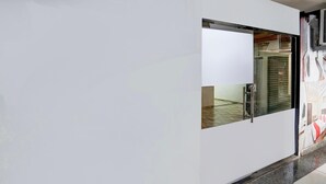 A modern hotel room with a large sliding door, a glass partition, and a tiled floor. - Super Hotel O Dindoli Surat (Surat)