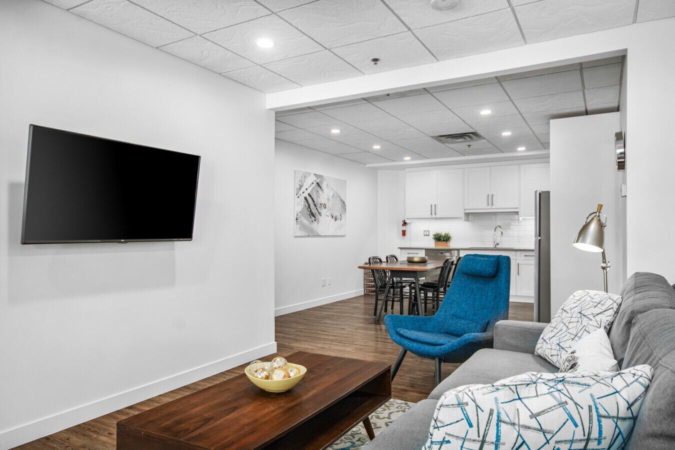 Een moderne woonkamer met een flatscreen televisie, een blauwe fauteuil, een grijze bank en een houten salontafel.