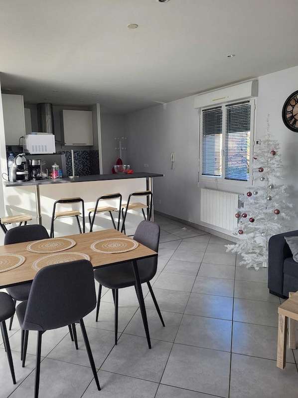 A modern kitchen with a dining area, a white Christmas tree, and a clock on the wall.
