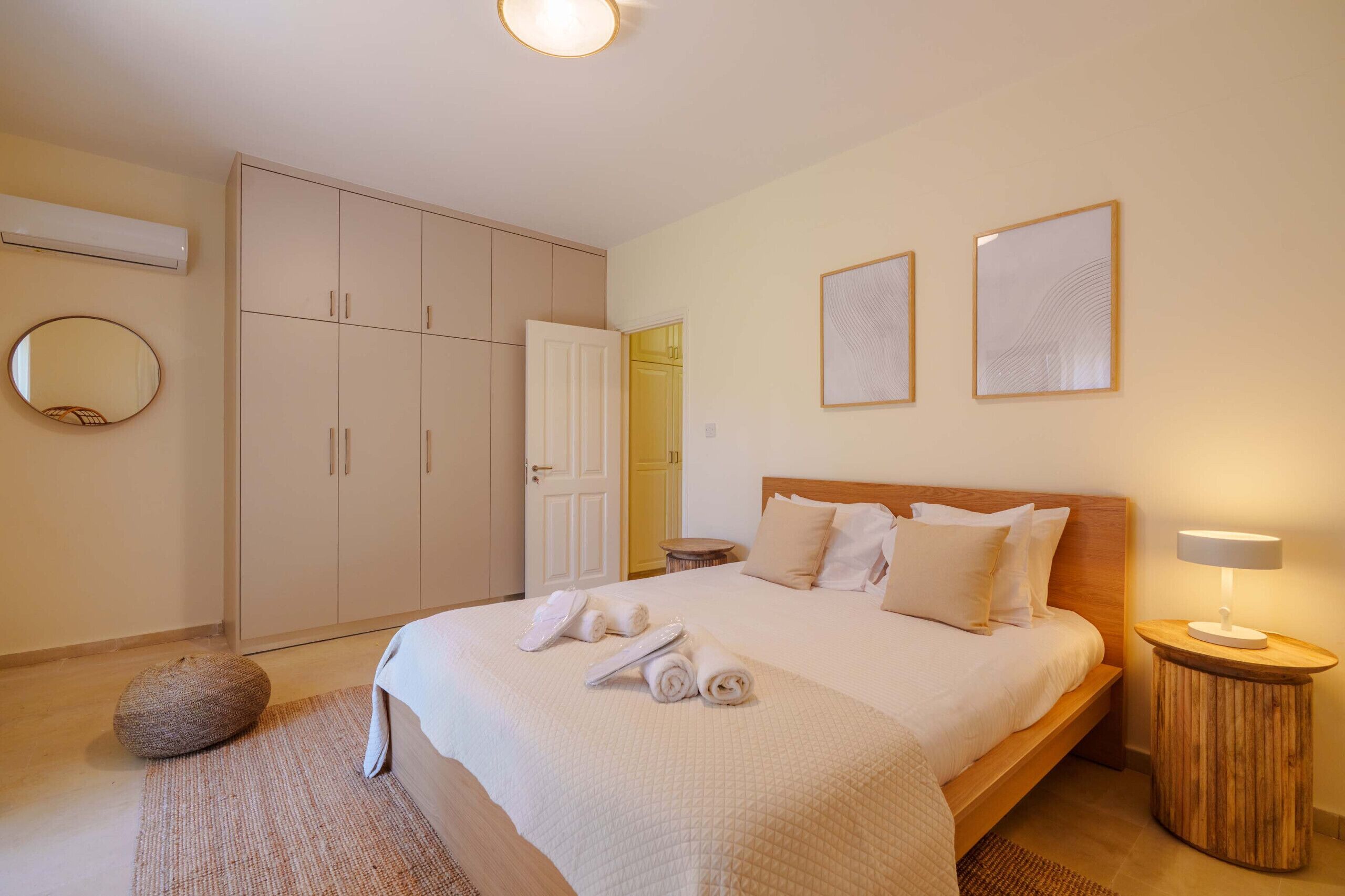 A bedroom with a bed, a wardrobe, a round mirror, and a bedside table with a lamp.