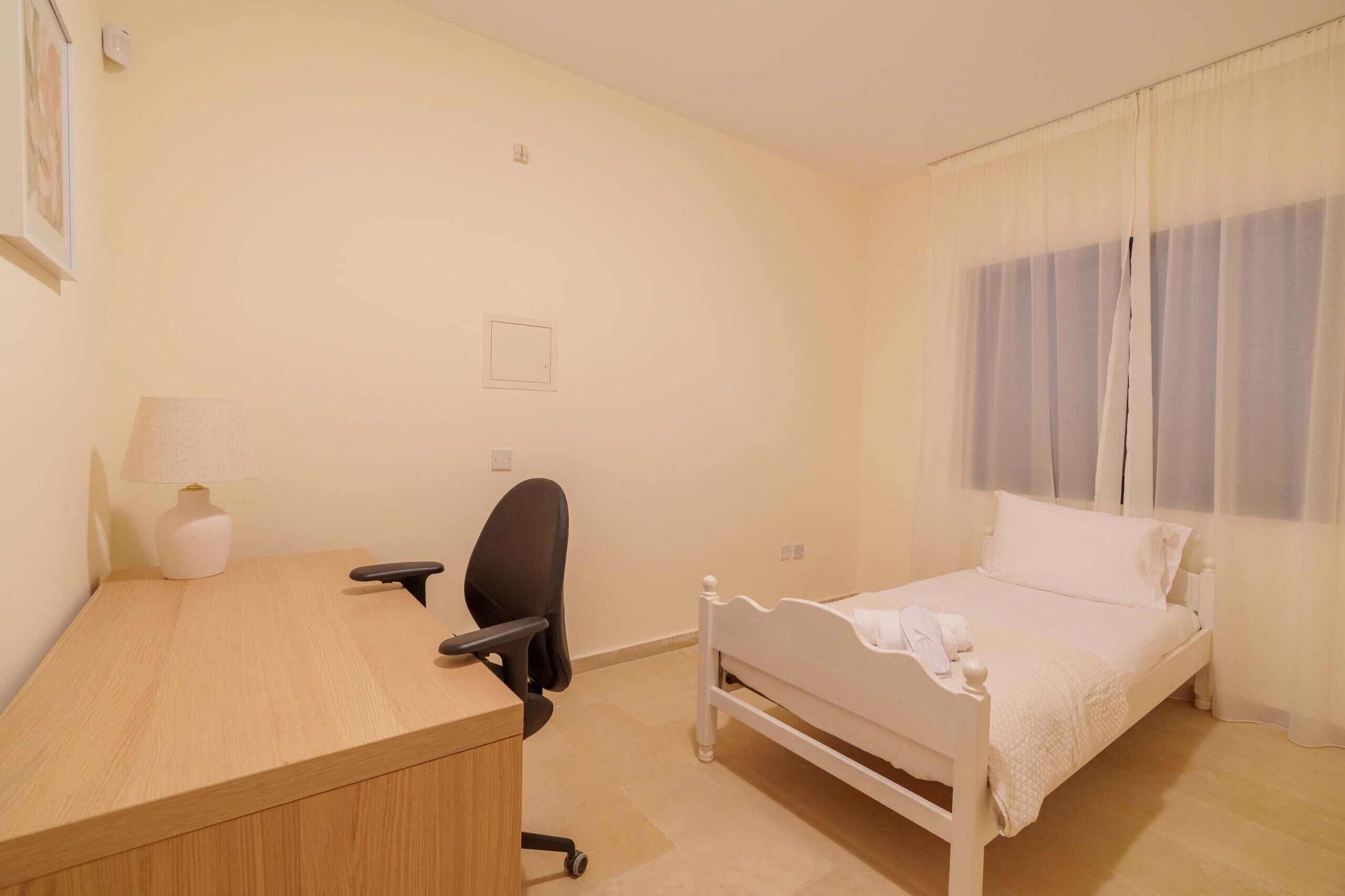 A bedroom with a bed, a desk, a chair, and a window with curtains.
