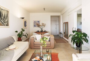 Una sala de estar con un sofá, una mesa de centro de vidrio, una mesa de comedor con sillas y plantas en macetas.