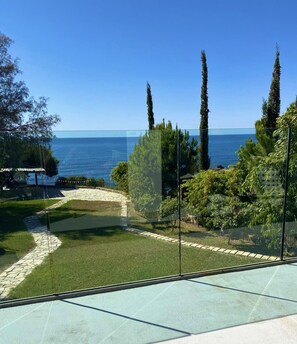 Vista desde un balcón sobre un jardín ajardinado con un sendero de piedra, un estanque pequeño y árboles altos.