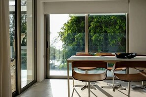 Un área de comedor con una mesa y sillas, un ventanal con vistas a la vegetación y un diseño interior moderno.