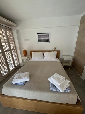 Un dormitorio con cama, dos mesitas de noche, un cuadro colgado en la pared y una ventana con persianas.