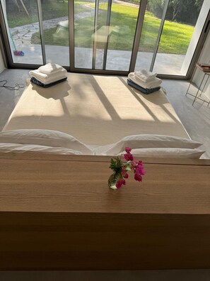 A room with a large bed, a small table with a vase of flowers, and a view of a garden through a glass door. - Pomos Villa - Stunning Views / Private Beach / Secluded (Pomos)