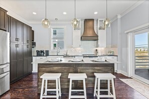 Una cocina moderna con armarios de madera oscura, una isla central con taburetes, iluminación colgante y un ventanal grande.