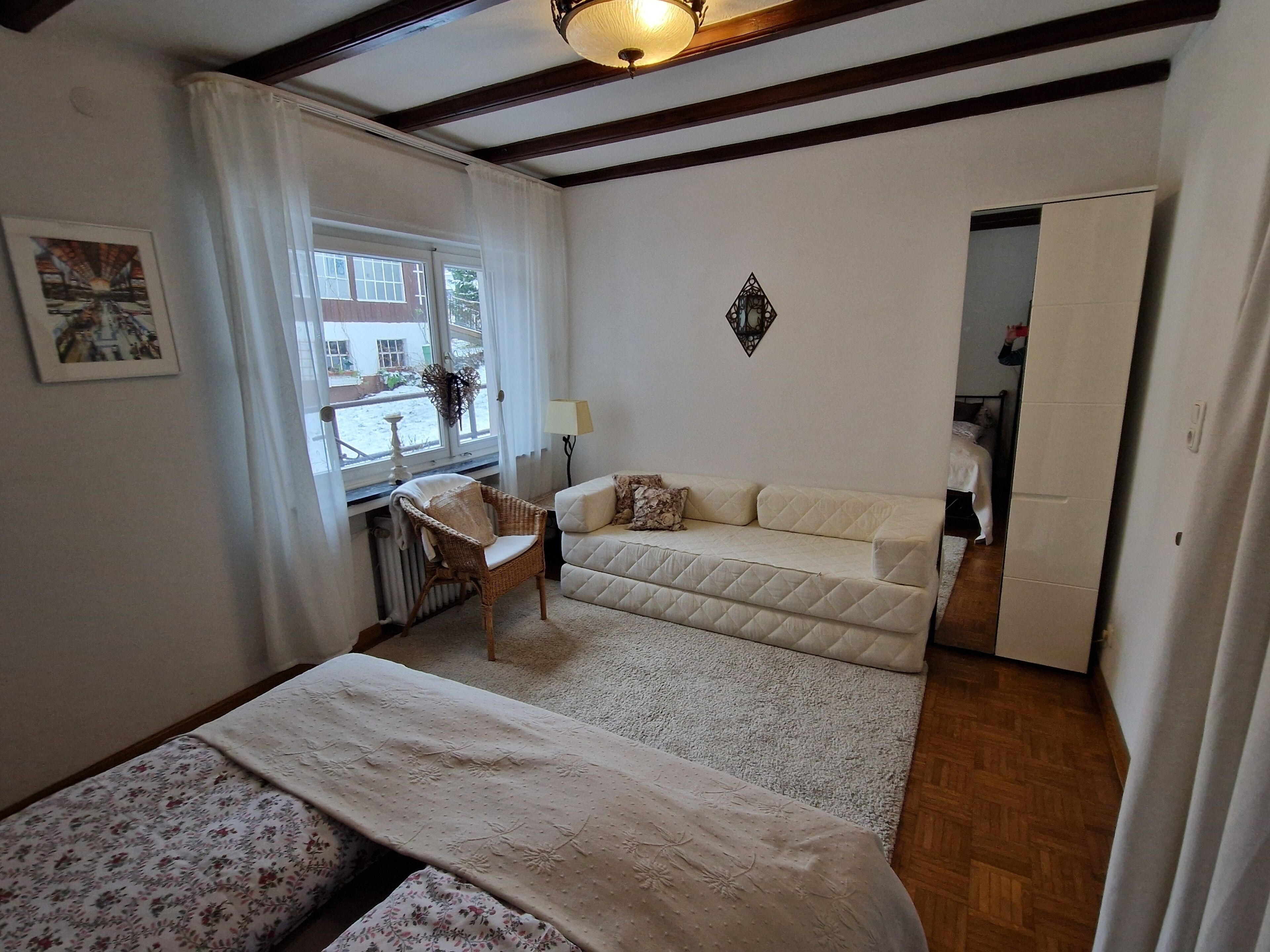 Een kamer met een bed, een stoel, een bank, een radiator, een raam en een deur.