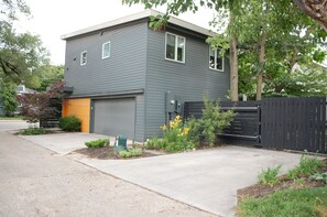 Ein modernes, zweistöckiges Haus mit Garage, schwarzem Zaun und gepflegtem Vorgarten mit Pflanzen und Blumen.