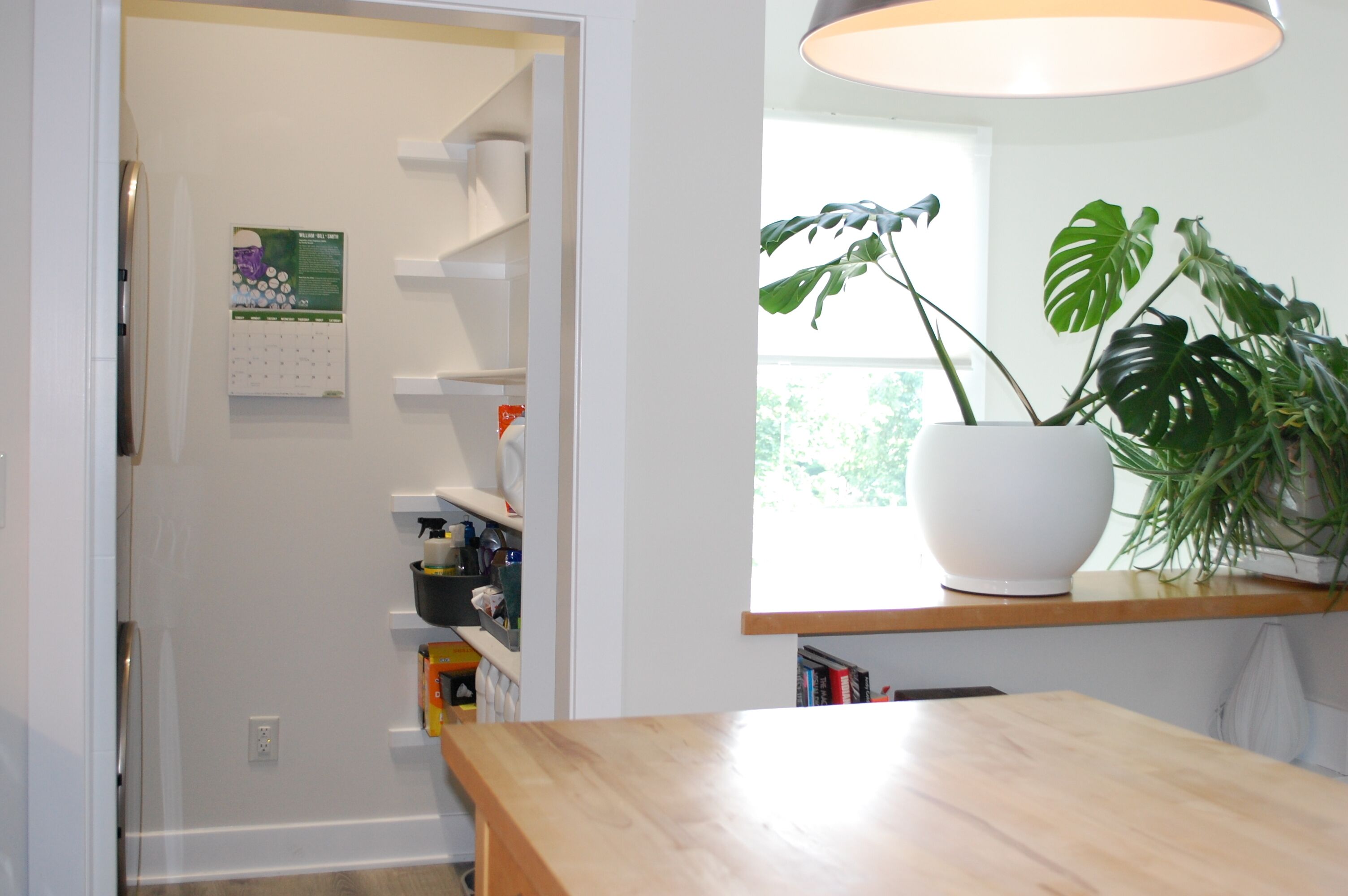 A kitchen with a wooden countertop, a potted plant, and a calendar on the wall.