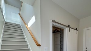 En trappe fører op til en loftsetage med gelænder i træ, et skydedørs skab og en dør med metalgreb.