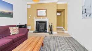 A living room with a fireplace, a sofa, a coffee table, and a hallway leading to another room. - The Drawing Room at The Merchants (Berwick-Upon-Tweed)