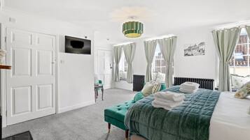 Une chambre d’hôtel avec un lit, une télévision, une fenêtre avec des rideaux, un radiateur et une chaise.