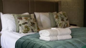 Una cama bien hecha con un edredón verde, almohadas blancas y una toalla doblada.