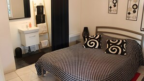 A bedroom with a bed, a bedside table, a mirror, a black and white patterned bedspread, and a wall art piece. - Guesthouse at the Rooster's Song (Saint-Lyé)