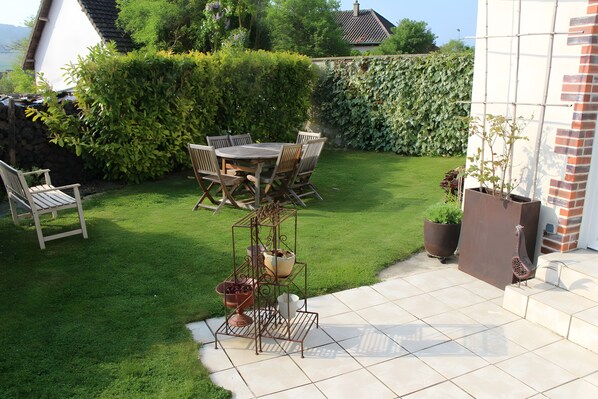 A patio with a table and chairs, a metal plant stand, and a potted plant.