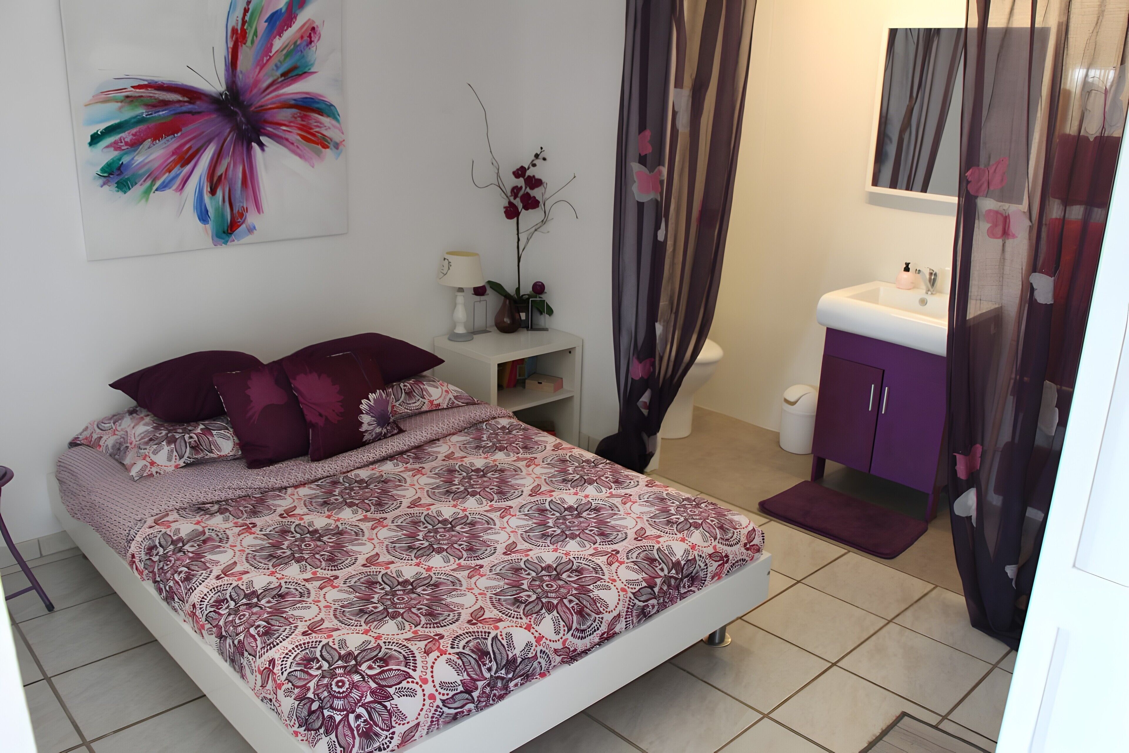 Une chambre à coucher comprenant un lit, une table de chevet, une commode, une salle de bain avec un lavabo et un rideau de douche.