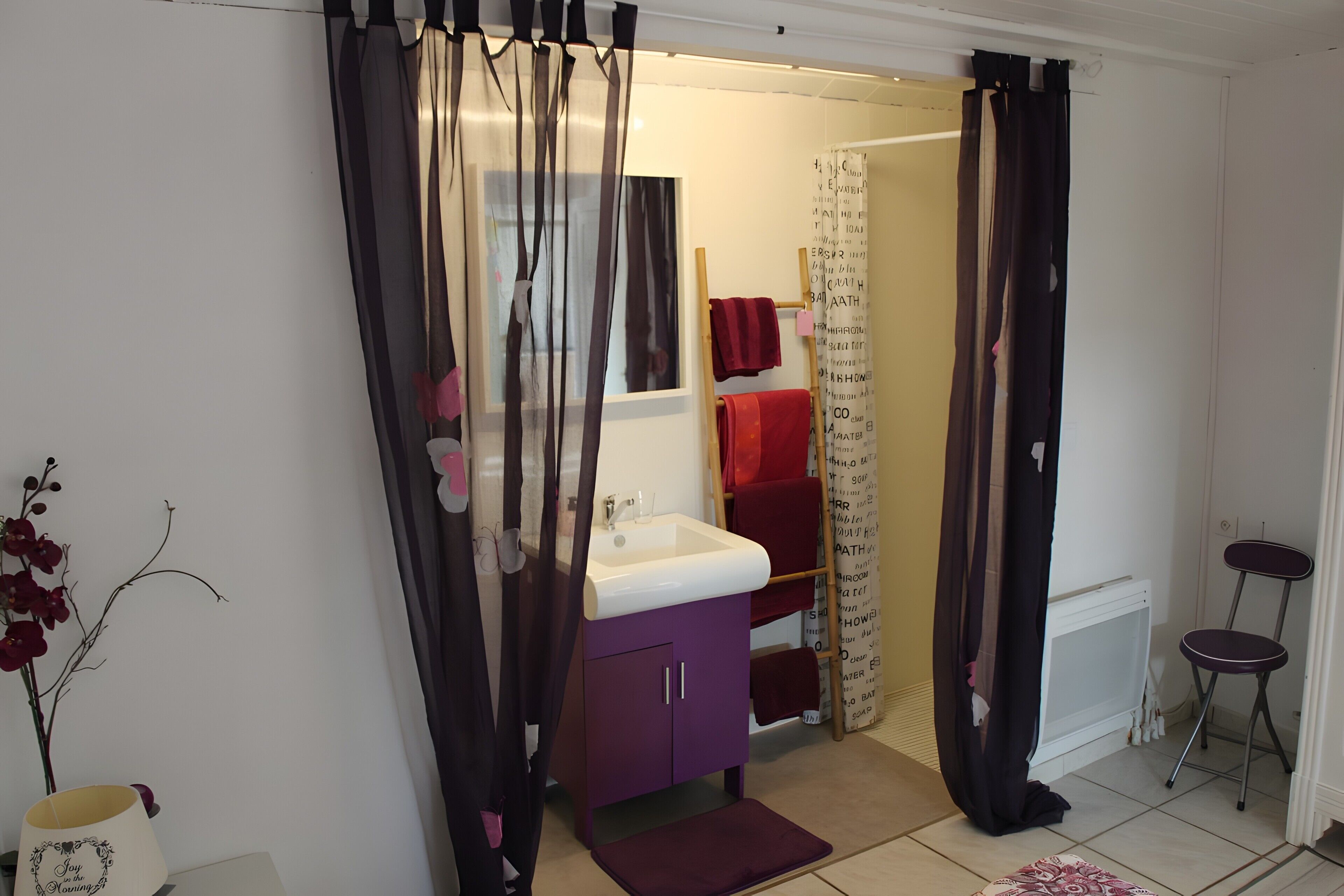 Casa de banho com toucador roxo, pia branca e porta-toalhas vermelho.