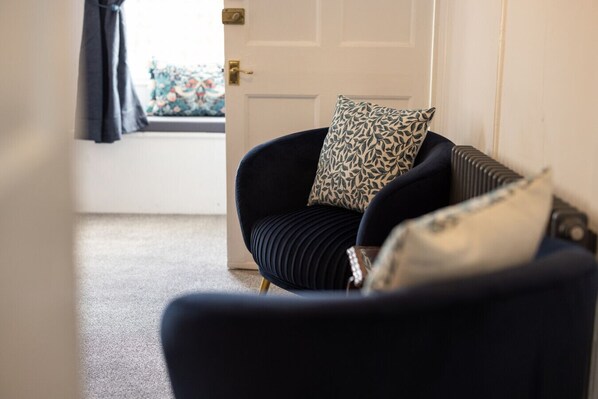 A dark blue armchair with a patterned pillow, a radiator, and a door leading to a room with a window.