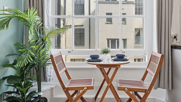 Een kamer met een raam, twee houten stoelen, een ronde tafel en een potplant.