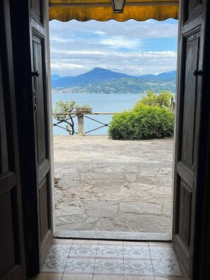 Eine offene Tür, die auf eine Steinterrasse mit Blick auf einen See und Berge führt.