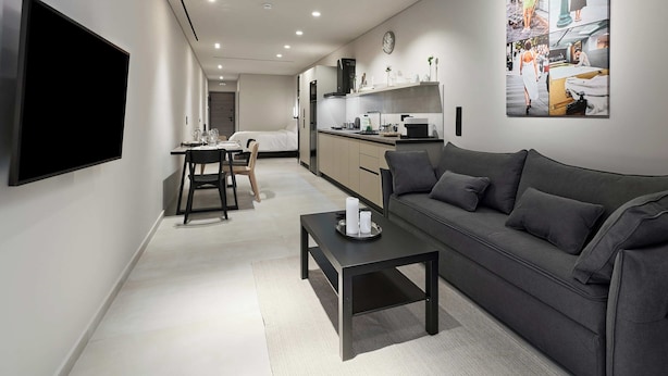 A modern living room with a flat-screen TV, a sofa, a coffee table, and a dining area with a table and chairs. - Moid Urban Suites (Athens)