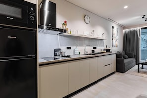 A modern kitchen with a black refrigerator, a microwave, and a stove. There is a clock on the wall and a window with curtains. - Moid Urban Suites (Athens)