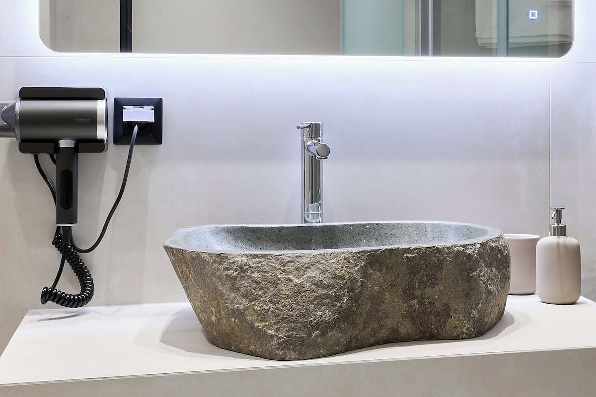 Un bagno moderno con un lavabo in pietra, uno specchio grande e un asciugacapelli a parete.