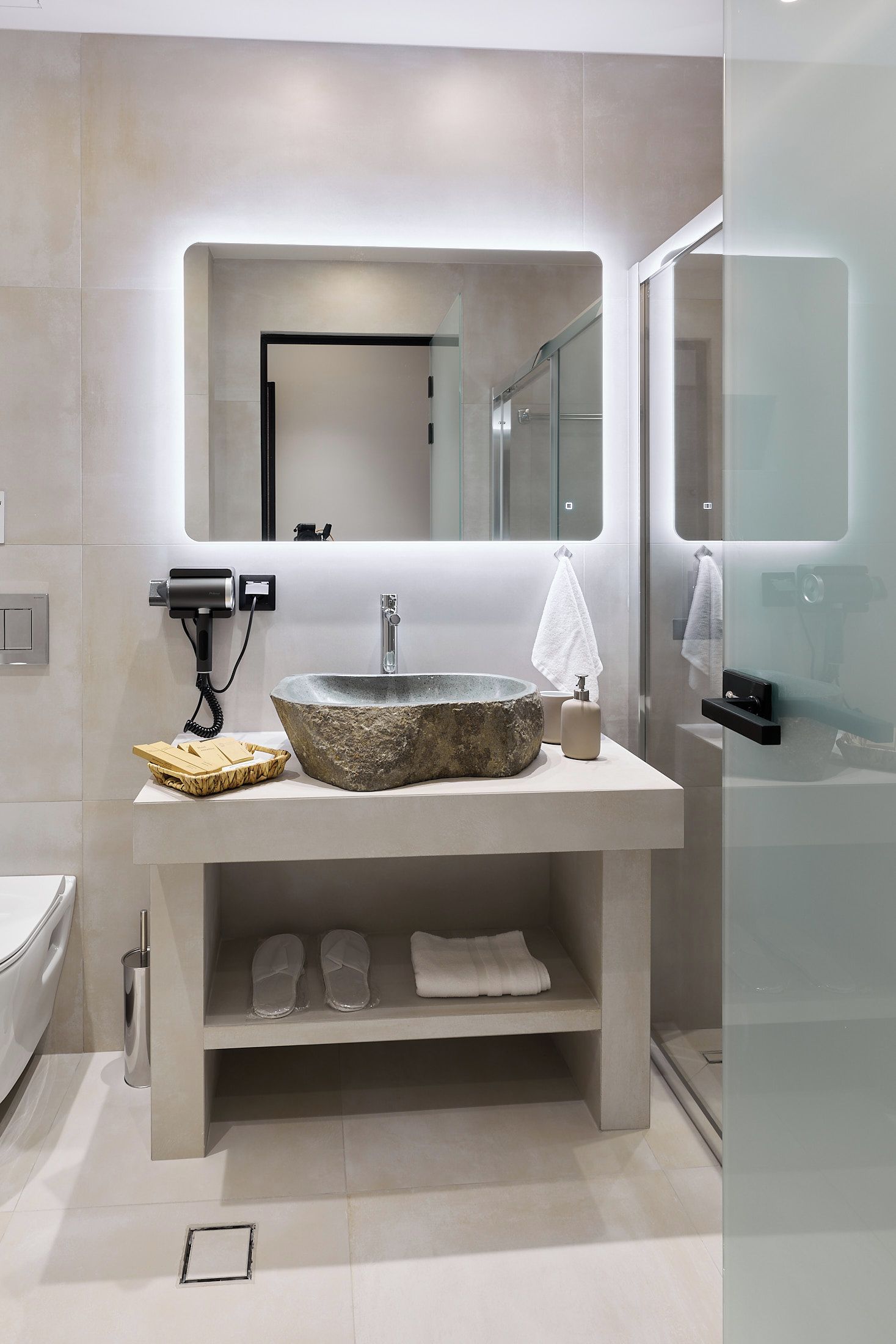 A modern bathroom with a stone sink, a hairdryer, and a glass shower enclosure.