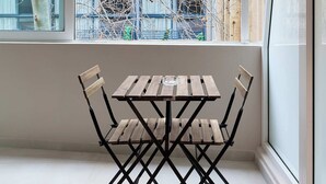 A dining area with a table and chairs, large windows, and a view of buildings and trees. - Moid Urban Suites (Athens)