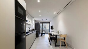 A modern kitchen with a built-in microwave and refrigerator, a dining area with a table and chairs, and a view through a glass door to an outdoor area. - Moid Urban Suites (Athens)