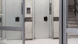 An interior view of a building with two doors, a digital display, and a tiled floor. - Moid Urban Suites (Athens)