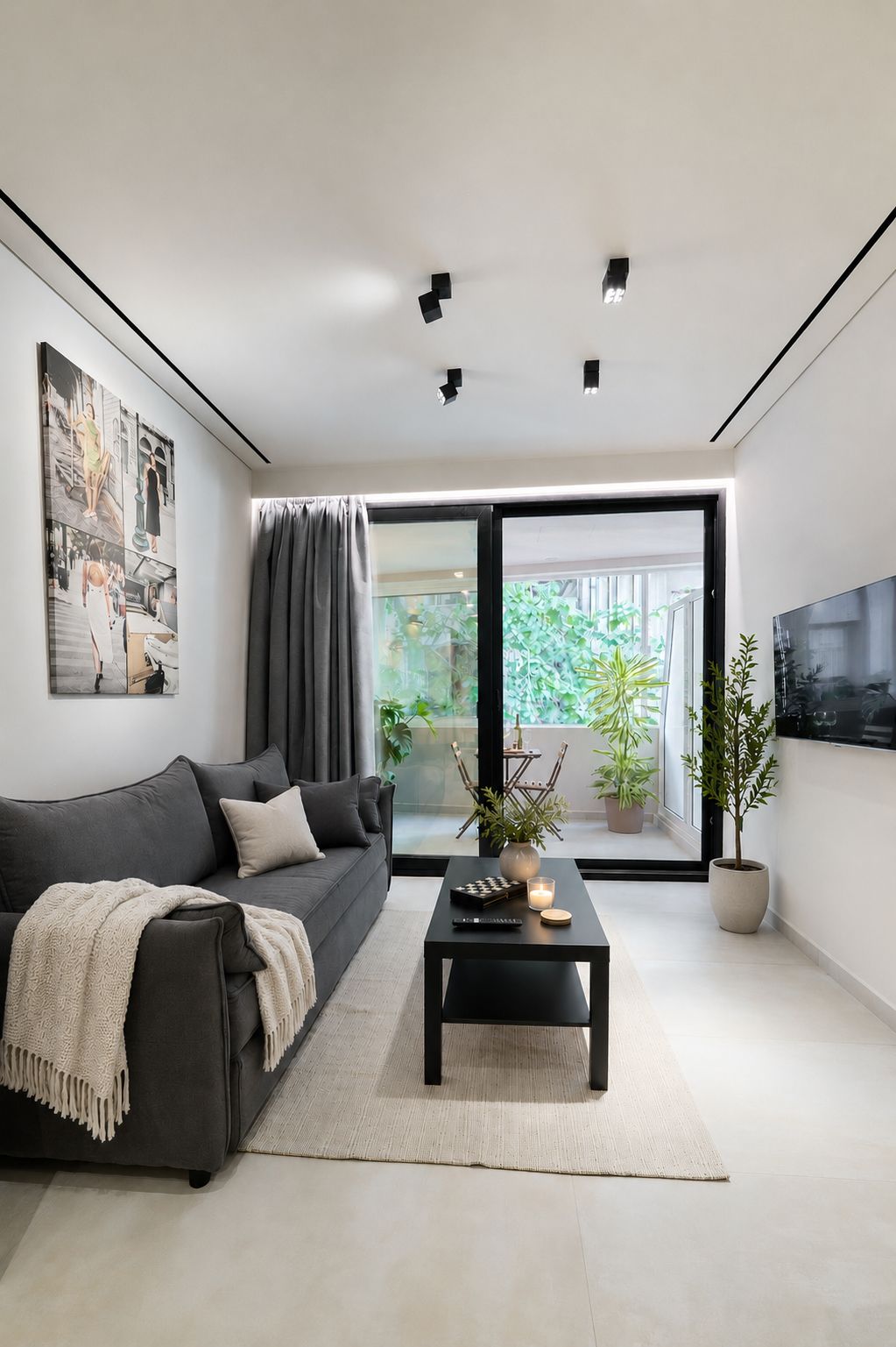 A modern living room with a dark grey sofa, a coffee table with a remote control, a candle, and a potted plant.