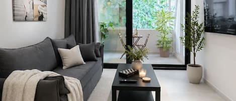 Un salon moderne avec un canapé gris foncé, une table basse avec une télécommande, une bougie et une plante en pot.