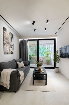 Een moderne woonkamer met een donkergrijze bank, een salontafel met een afstandsbediening, een kaars en een potplant.