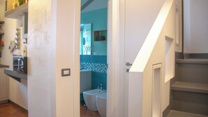 A kitchen with a refrigerator, microwave, and shelves with items. A bathroom with a toilet and sink is visible through an open door. - Casa Zeda WelcHome (Intra)
