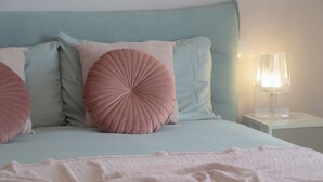A bed with a teal headboard, multiple pillows, a bedside lamp, and a pink blanket. - Casa Zeda WelcHome (Intra)