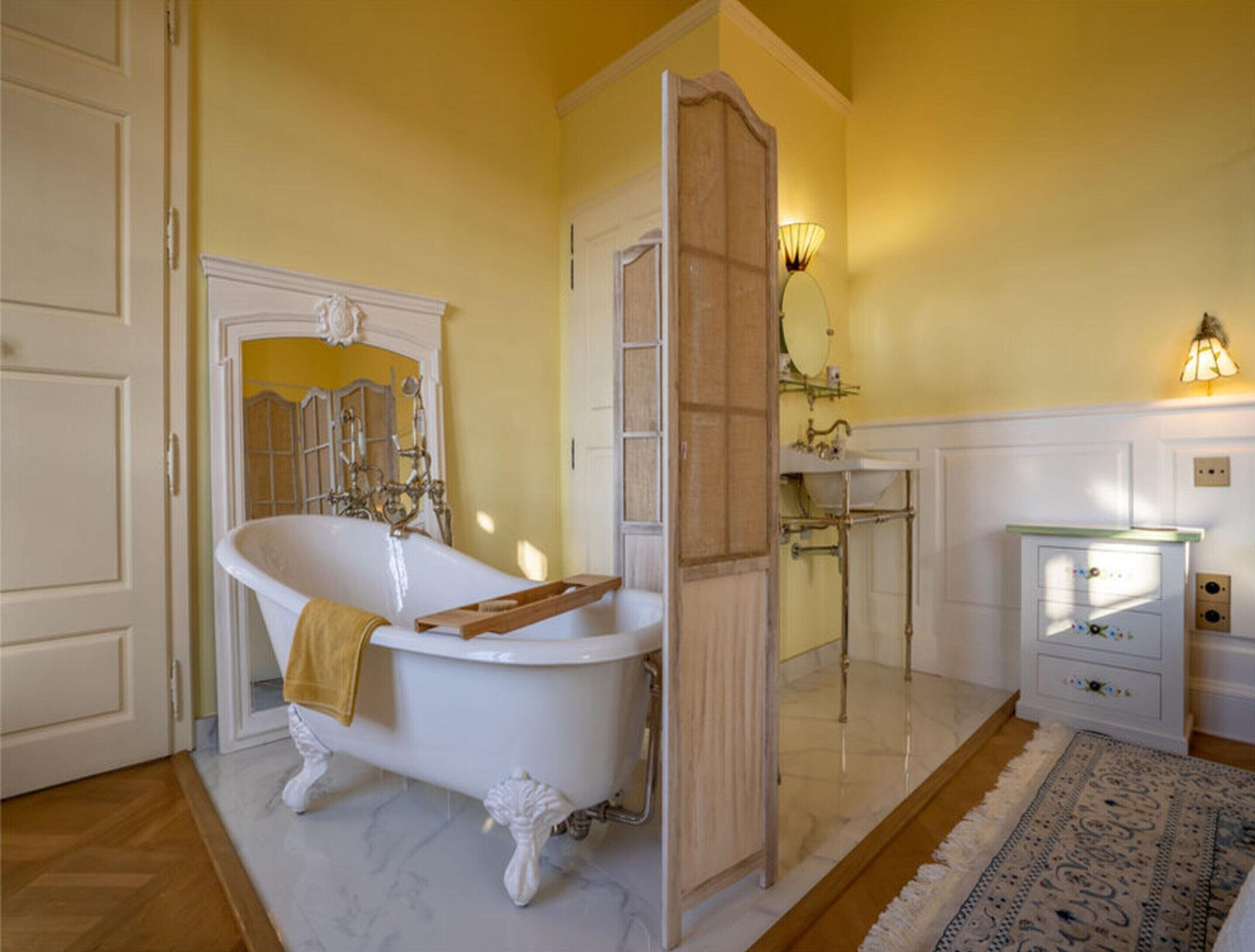 A bathroom with a white clawfoot bathtub, a wooden shelf, a mirror, and a sink with a decorative cabinet.