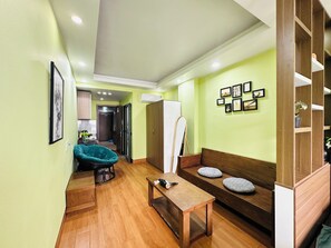 A room with a wooden bench, a small table, a green wall with framed pictures, and a whiteboard. - Ann's Homestay Ngoai Giao Doan (Ha Noi)