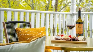 A wooden chair with a yellow cushion, a white railing, a bottle of wine, and a glass on a small table with a cheese board. - Maine Social House/By Downtown/Balcony (Portland)