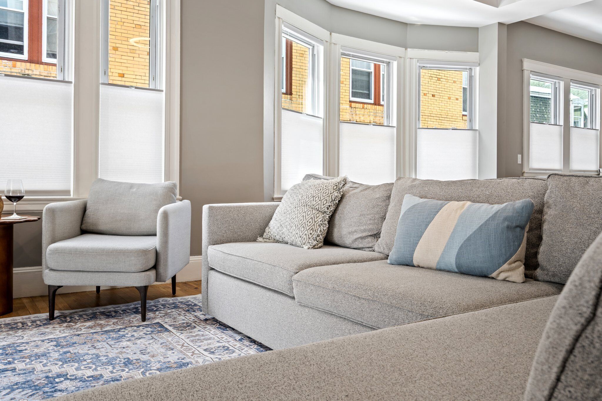 A living room with a grey sofa, a grey armchair, and a patterned rug.