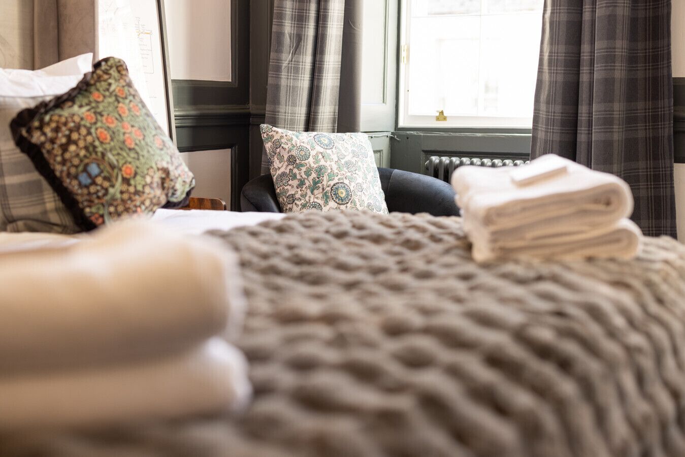 A bed with a knitted blanket, two patterned pillows, and a stack of folded towels.