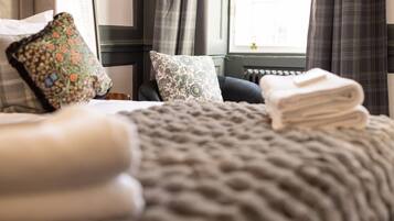 A bed with a knitted blanket, two patterned pillows, and a stack of folded towels.