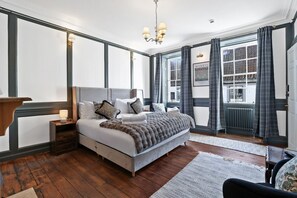 A bedroom with a large bed, a nightstand, a dresser, a chandelier, and a window with curtains.