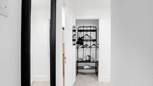 Pasillo que conduce a una habitación con un perchero metálico negro y una pequeña mesa con una tetera y tazas.