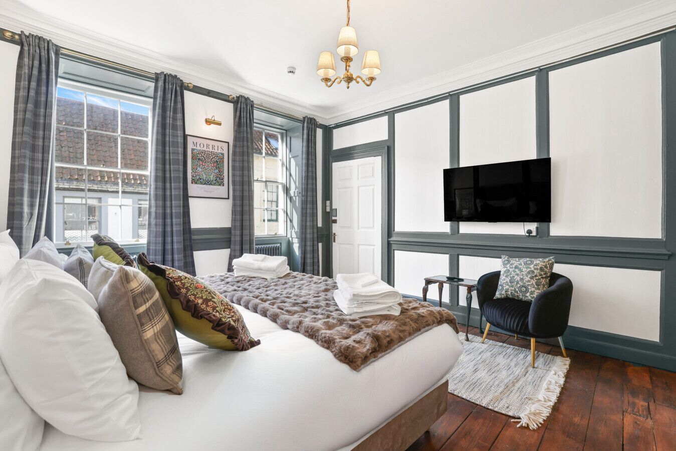 A hotel room with a large bed, a flat-screen TV, a chair, and a view of the city.